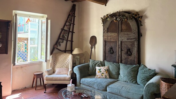 A cozy living room with a wooden ceiling, a green sofa, a white armchair, and a ladder leaning against the wall.