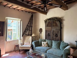 A cozy living room with a wooden ceiling, a green sofa, a white armchair, and a ladder leaning against the wall. - Casa Baldecchi - Pistoia Centro Storico (Pistoia)