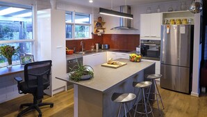 A modern kitchen with a central island, stainless steel appliances, and a bar stool seating arrangement. - Oasis in Aldinga Beach, an affordable holiday near the beach (Aldinga Beach)
