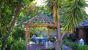 A wooden pergola with a table and chairs, surrounded by lush greenery and plants. - Oasis in Aldinga Beach, an affordable holiday near the beach (Aldinga Beach)