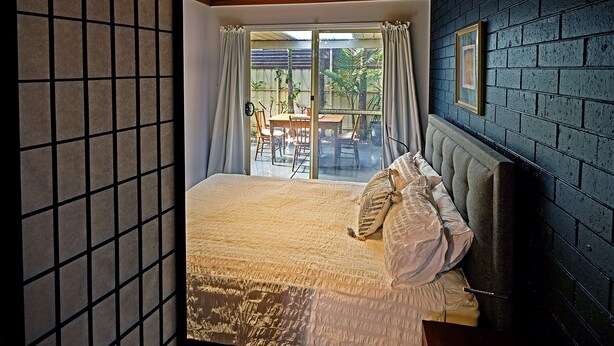 A bedroom with a large bed, a view of the outside patio, and a dark brick wall. - Oasis in Aldinga Beach, an affordable holiday near the beach (Aldinga Beach)