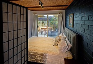 A bedroom with a large bed, a view of the outside patio, and a dark brick wall. - Oasis in Aldinga Beach (Aldinga Beach)