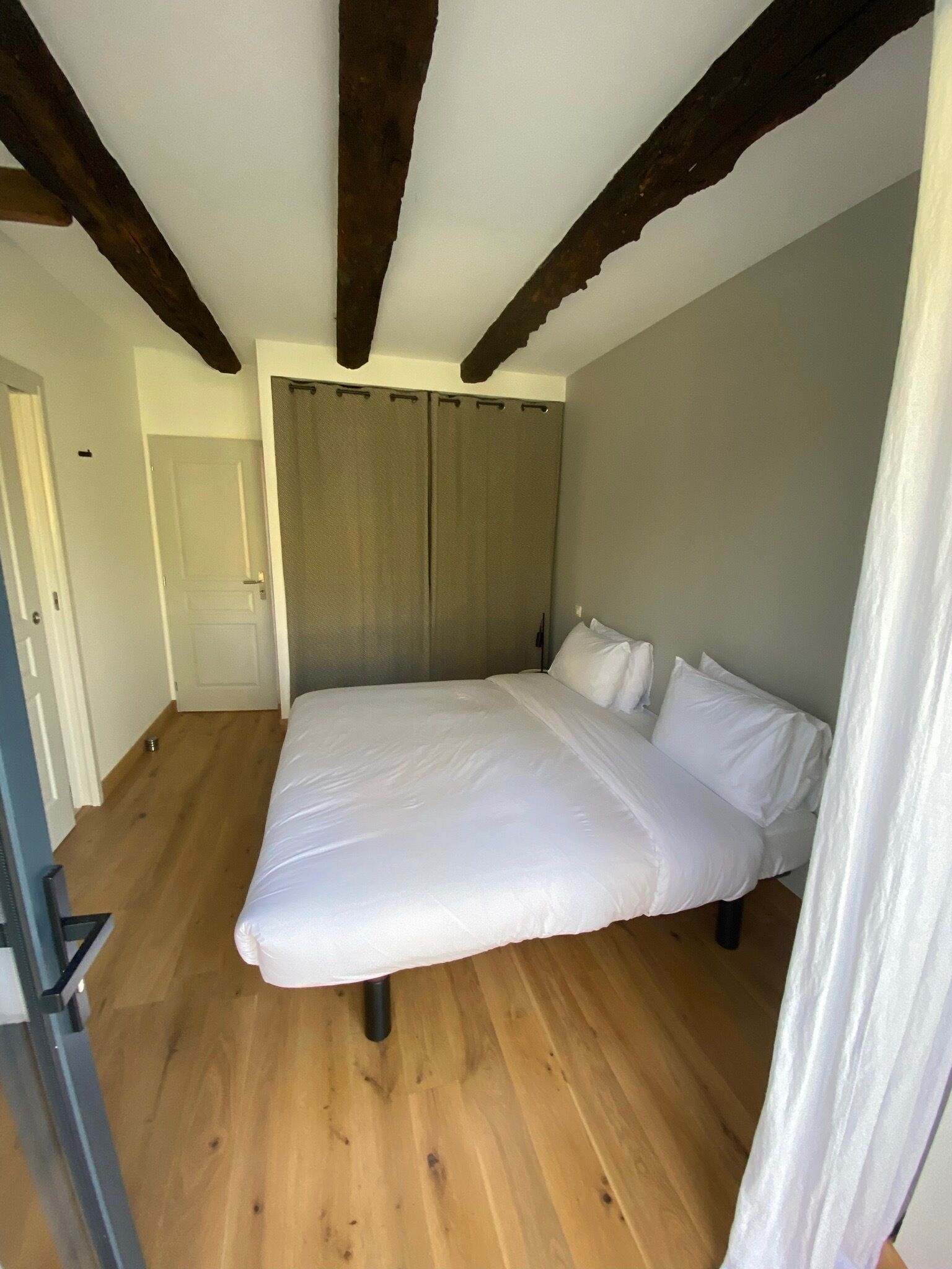 Un dormitorio con una cama grande, vigas de madera en el techo y una pared gris.