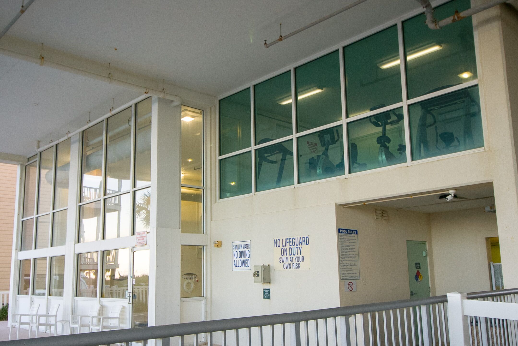 A building with large windows, a pool area, and signs indicating no lifeguard on duty and shallow water no diving allowed.