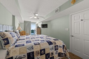Un dormitorio con una cama grande, un ventilador de techo, un televisor en la pared y una puerta.