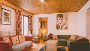 A cozy living room with a red sofa, a green sofa, and a wooden coffee table. There is a painting on the wall and a window with curtains.