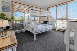 A bunk bed room with a view of the outdoors, a small table with a lamp, and a plant.