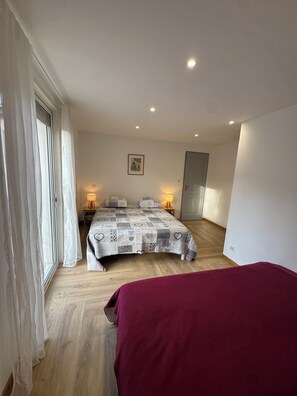 A bedroom with a bed, two bedside tables, a window with curtains, and a door.