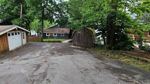 A residential driveway leading to a house with a garage, surrounded by trees and a wooden fence.