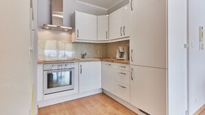 Una cocina moderna con armarios blancos, horno integrado y una encimera con cafetera.