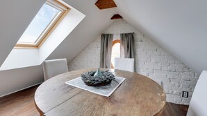 Um quarto de sótão aconchegante com teto inclinado, uma mesa de madeira redonda e um lustre rústico como peça central.
