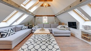 Um quarto estilo loft com teto alto, vigas de madeira aparentes, uma janela ampla e um espaço de estar acolhedor com sofá e mesa de centro.
