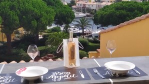 A table set with a bottle, two glasses, and plates with "Bon Appetit" written on them, overlooking a marina with boats and greenery. - Loft style apartment with Solarium on the last Floor (Cap d'Agde)