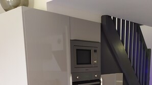A kitchen with a built-in microwave and oven, a staircase with a dark railing, and tiled flooring. - Loft style apartment with Solarium on the last Floor (Cap d'Agde)