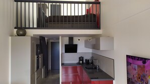 A modern kitchen with a red countertop, black appliances, and a black staircase leading to a balcony. - Loft style apartment with Solarium on the last Floor (Cap d'Agde)