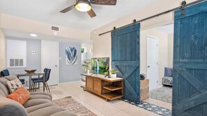 A living room with a sofa, a coffee table, and a TV. There is a sliding barn door and a door leading to another room.