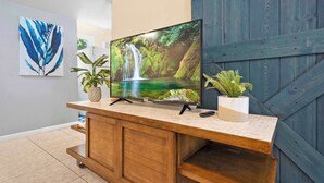 A wooden TV stand with a flat-screen TV displaying a waterfall scene, two potted plants, and a framed artwork on the wall.