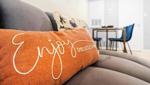 A close-up of a sofa with a cushion that reads "Enjoy THE LITTLE THINGS."