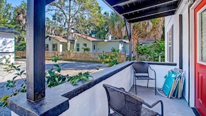 A covered patio with two wicker chairs, a red door, and a view of neighboring houses.