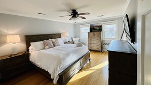 Een slaapkamer met een bed, nachtkastjes, een dressoir, een plafondventilator en een aan de muur bevestigde televisie.