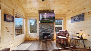 A cozy cabin interior with a stone fireplace, a comfortable armchair, and a television. - Mountain and City light views! Close to Strip, Private Indoor Pool + Free Tix (Pigeon Forge)