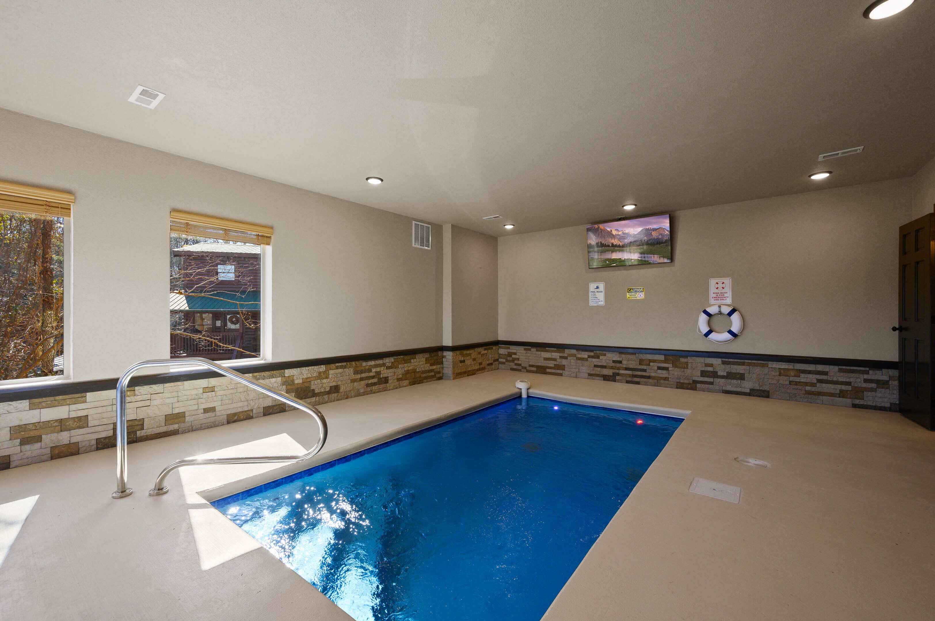A swimming pool with a metal ladder, beige walls, a tiled border, and a window with blinds.