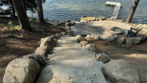 Ein Steinweg führt zu einem Steg an einem See, umgeben von großen Felsen und Bäumen.