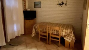 Habitació petita amb un llit, una televisió sobre un suport, una làmpada de paret i una finestra amb cortines.