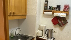 Una cuina petita amb armaris de fusta, un rentaplats, un obrador, una cafetera i una petita estant amb diversos objectes.