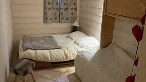 Un dormitori petit i acollidor amb un llit, un tamboret i una finestra amb cortines.