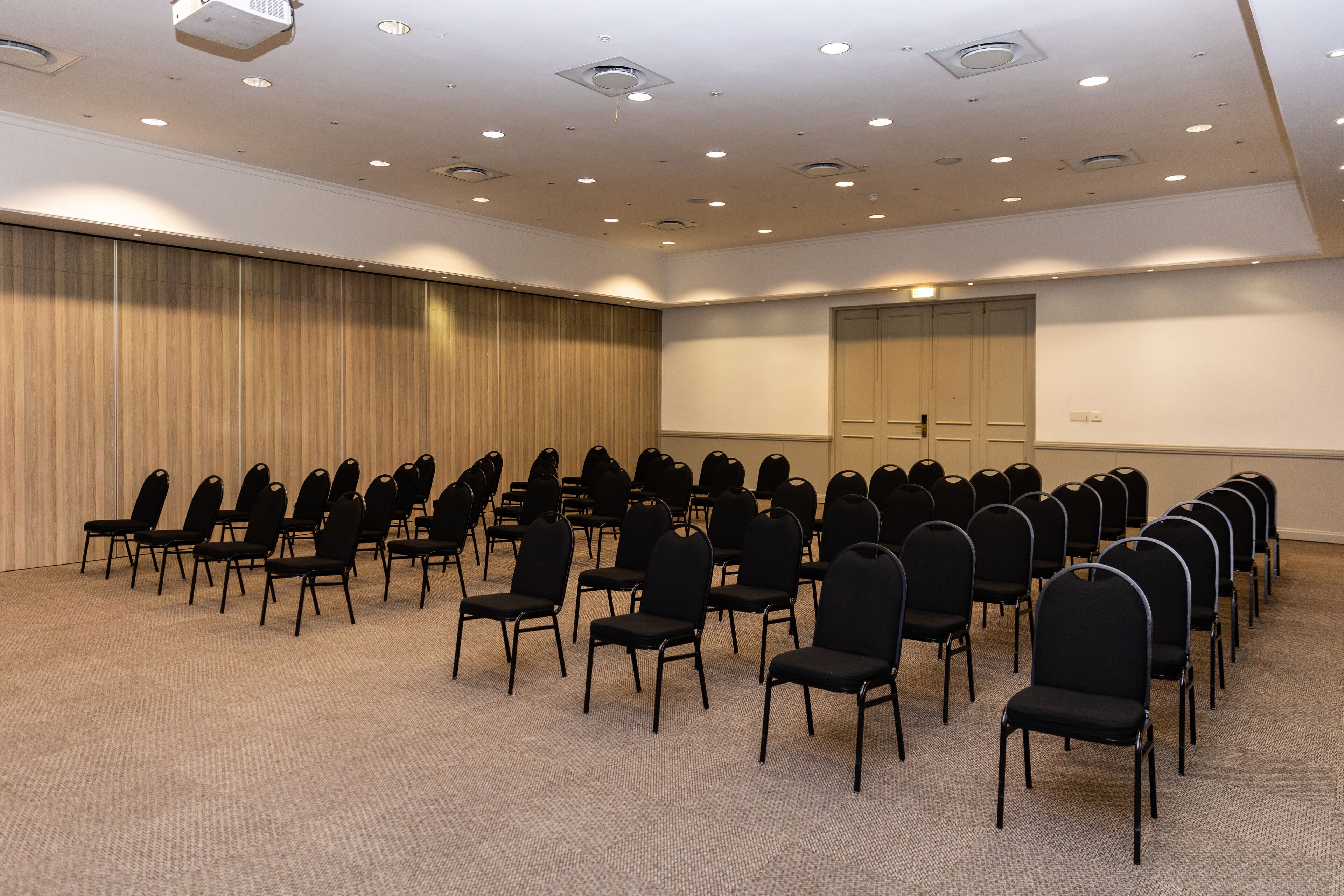 A conference room with rows of black chairs, a carpeted floor, and a whiteboard on the wall.