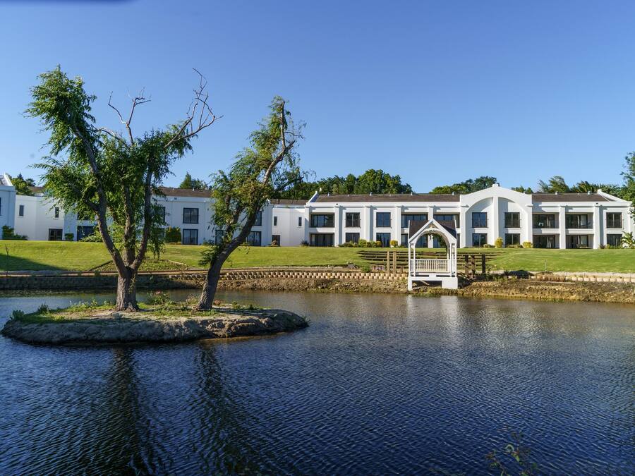 A large building with a pond in front, surrounded by trees and a well-maintained lawn.