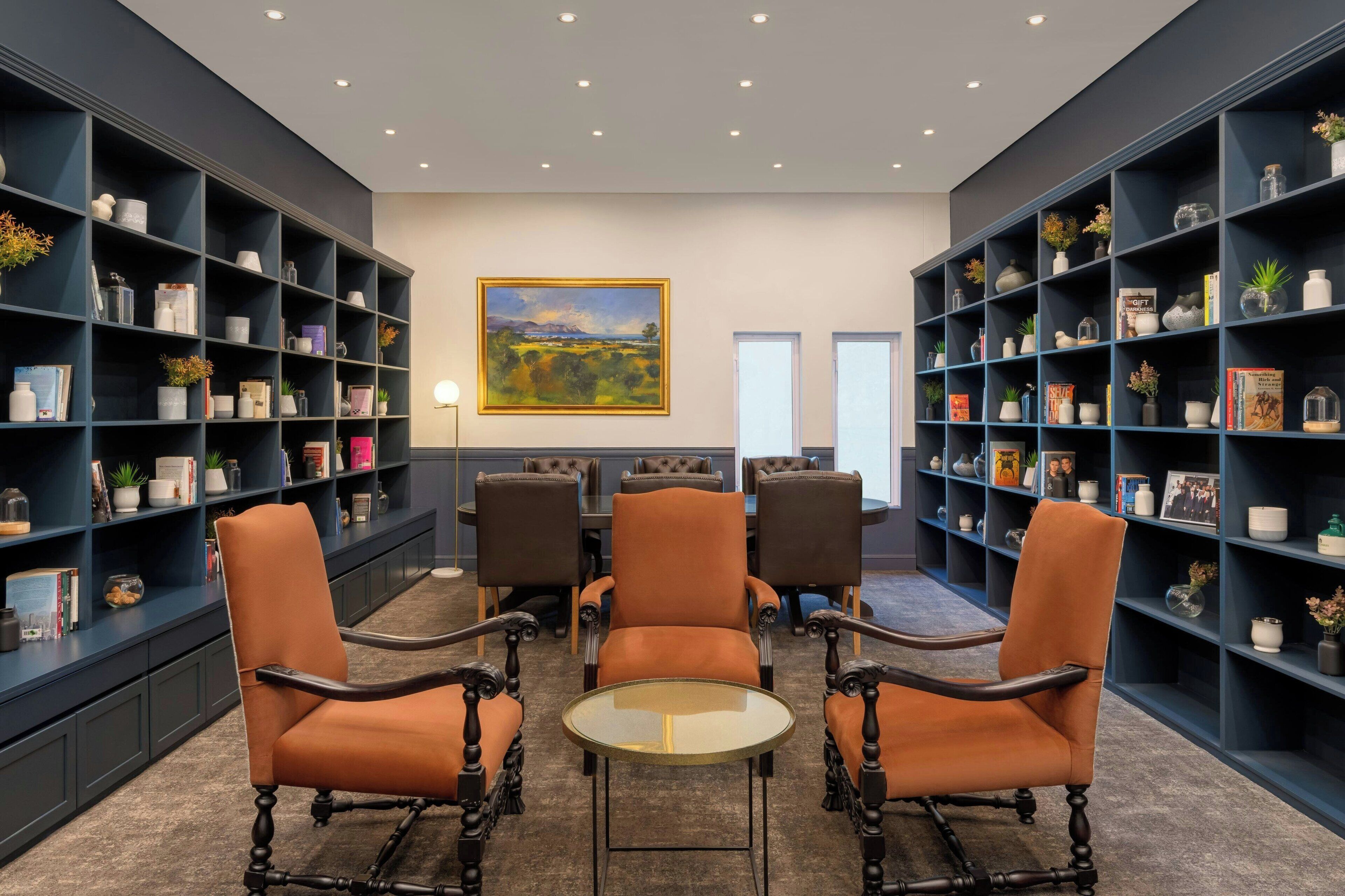 Una biblioteca con estanterías azul oscuro, una mesa redonda y cuatro sillones de cuero.