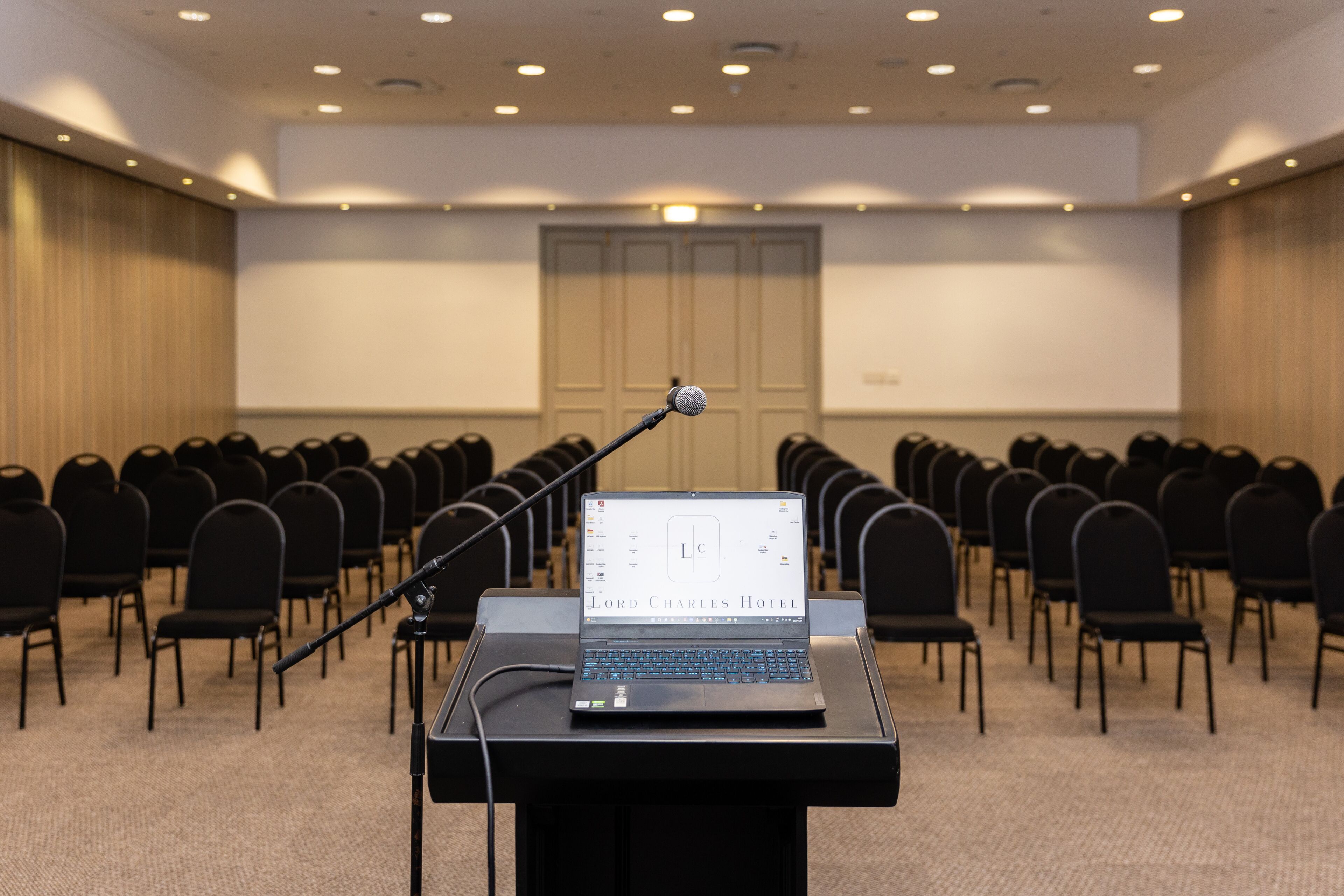 A conference room with rows of chairs, a podium with a laptop, and a projection screen.