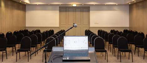 A conference room with rows of chairs, a podium with a laptop, and a projection screen.