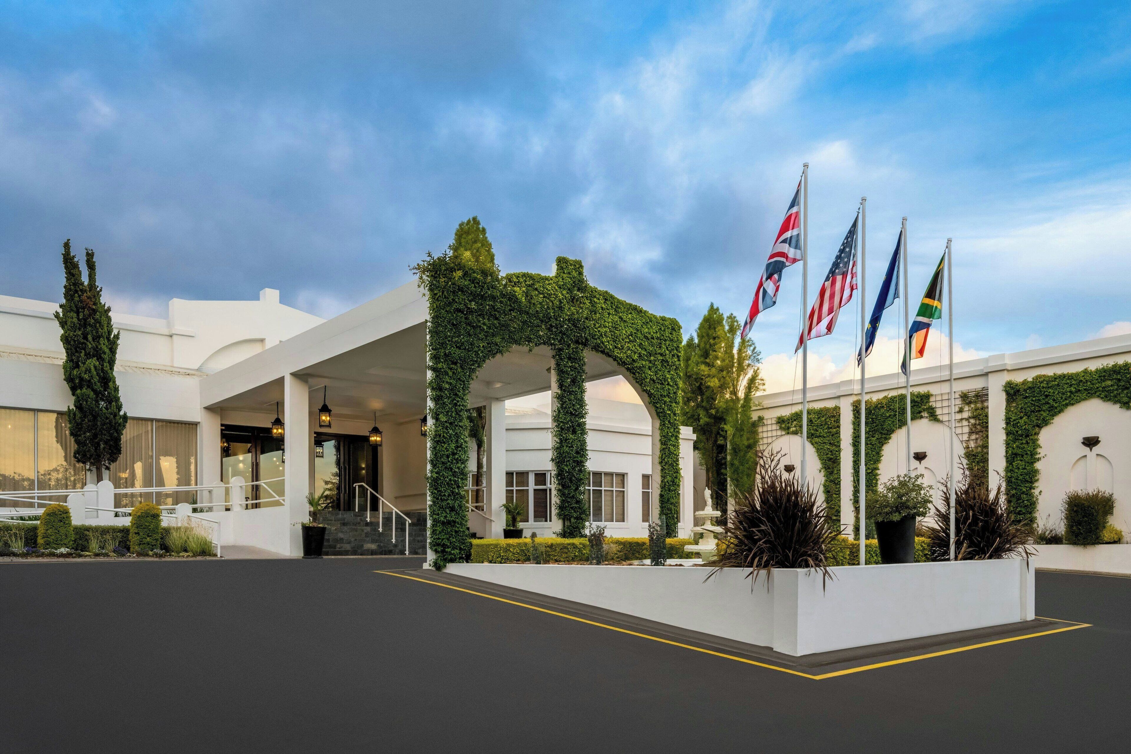 Een hotel ingang met een overdekte gangpad, vlaggen en beplanting.