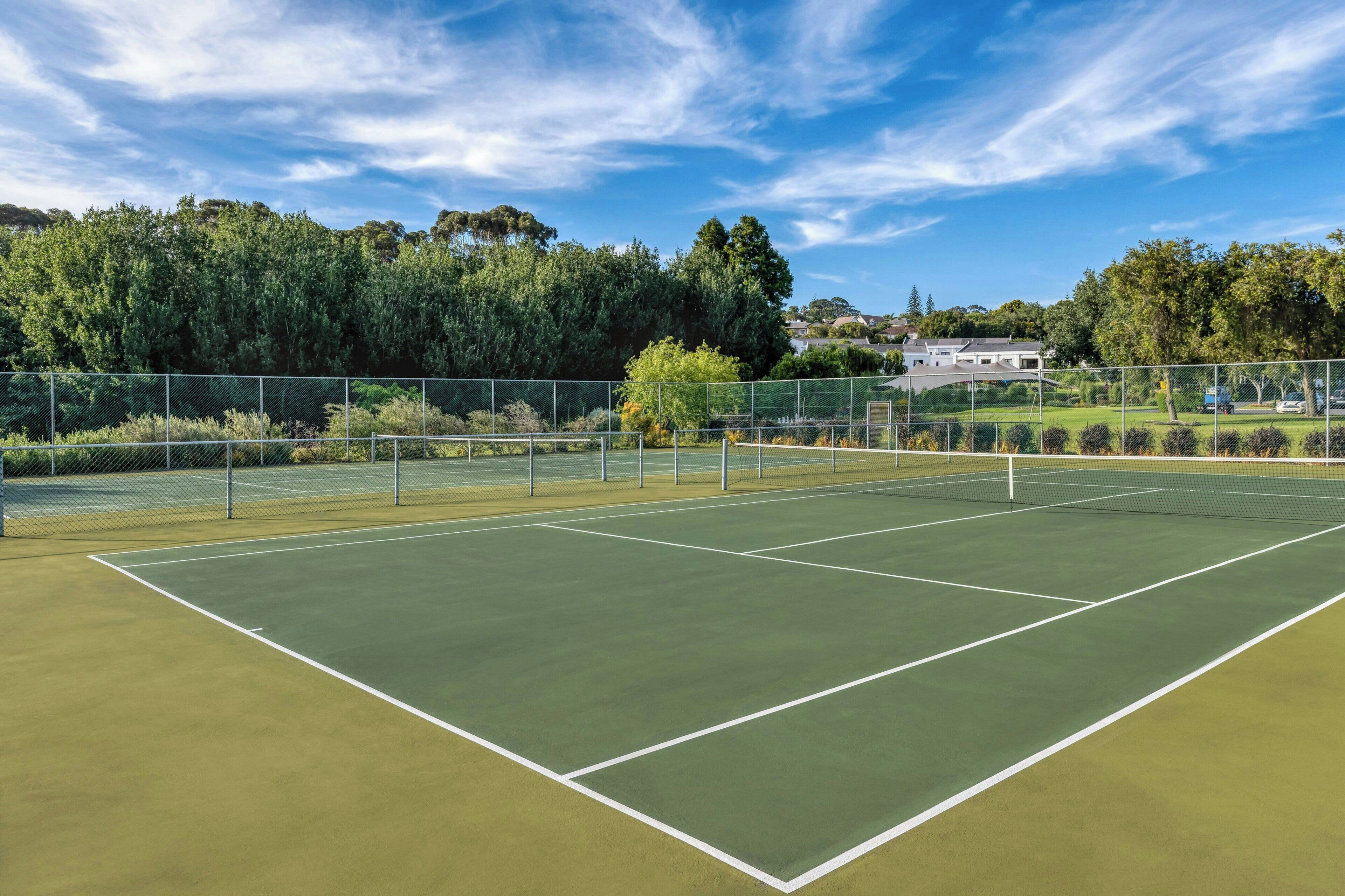 Ein Tennisplatz mit Netz, umgeben von einer Hecke und Bäumen.