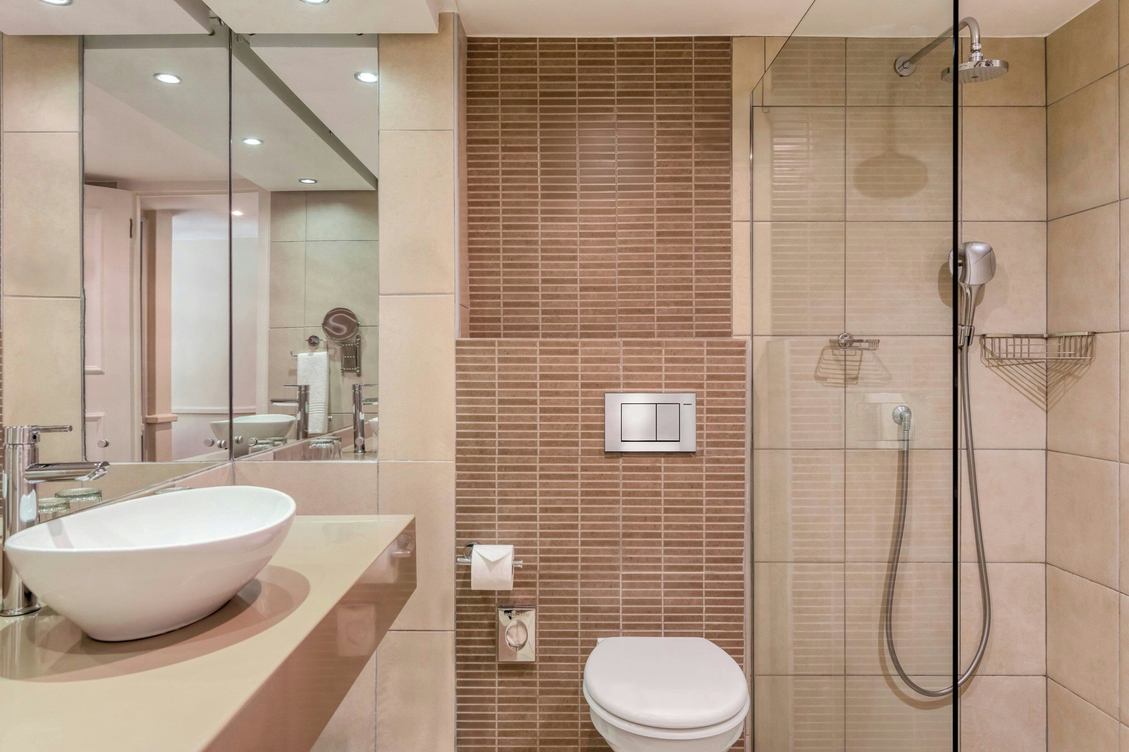 A modern bathroom with a large white sink, a toilet, and a glass-enclosed shower area.