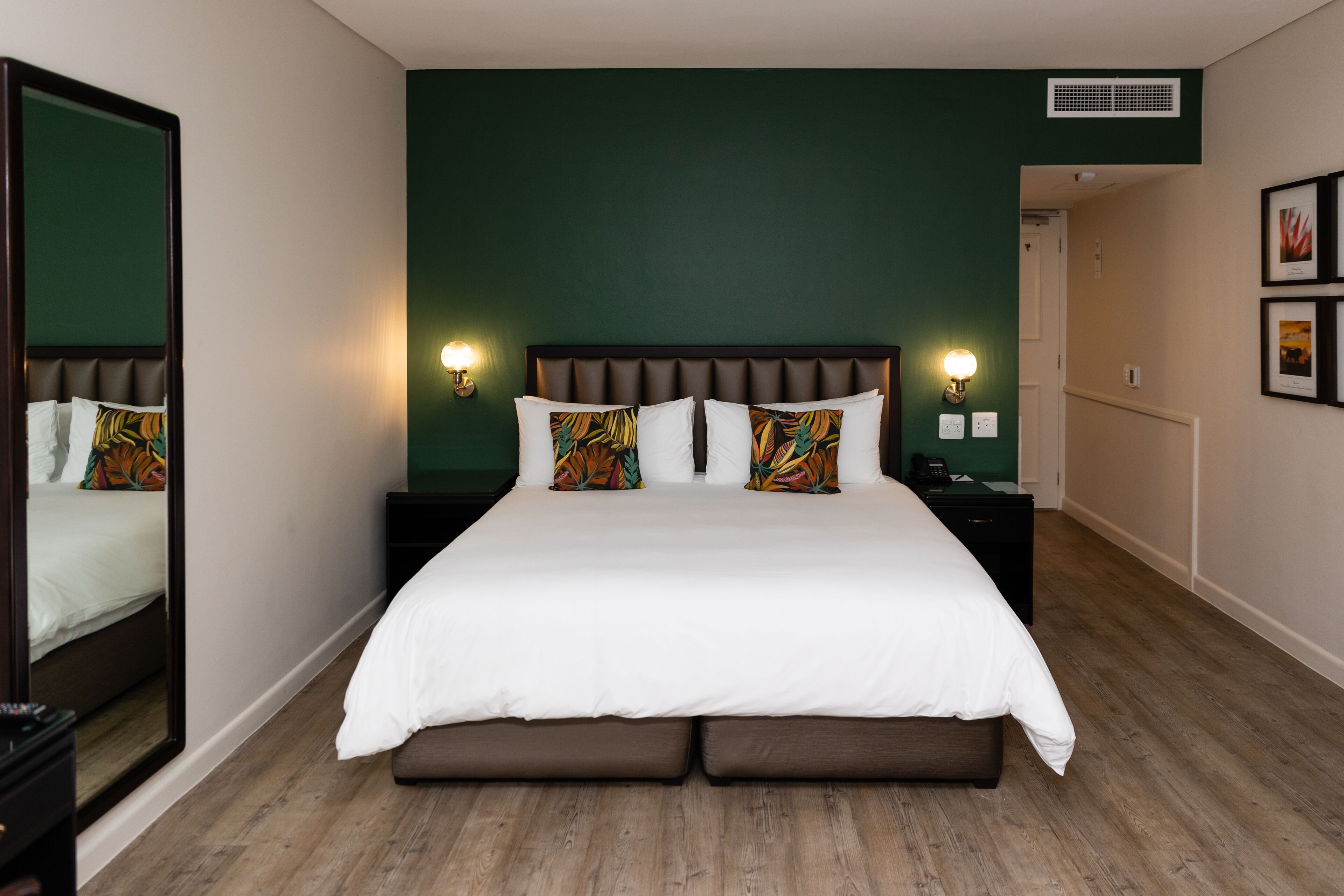 Habitación de hotel con una cama grande, dos mesitas de noche, un espejo y una pared de acento verde.