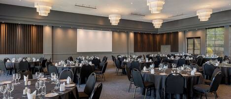 A conference room with multiple tables, black chairs, and overhead lighting.