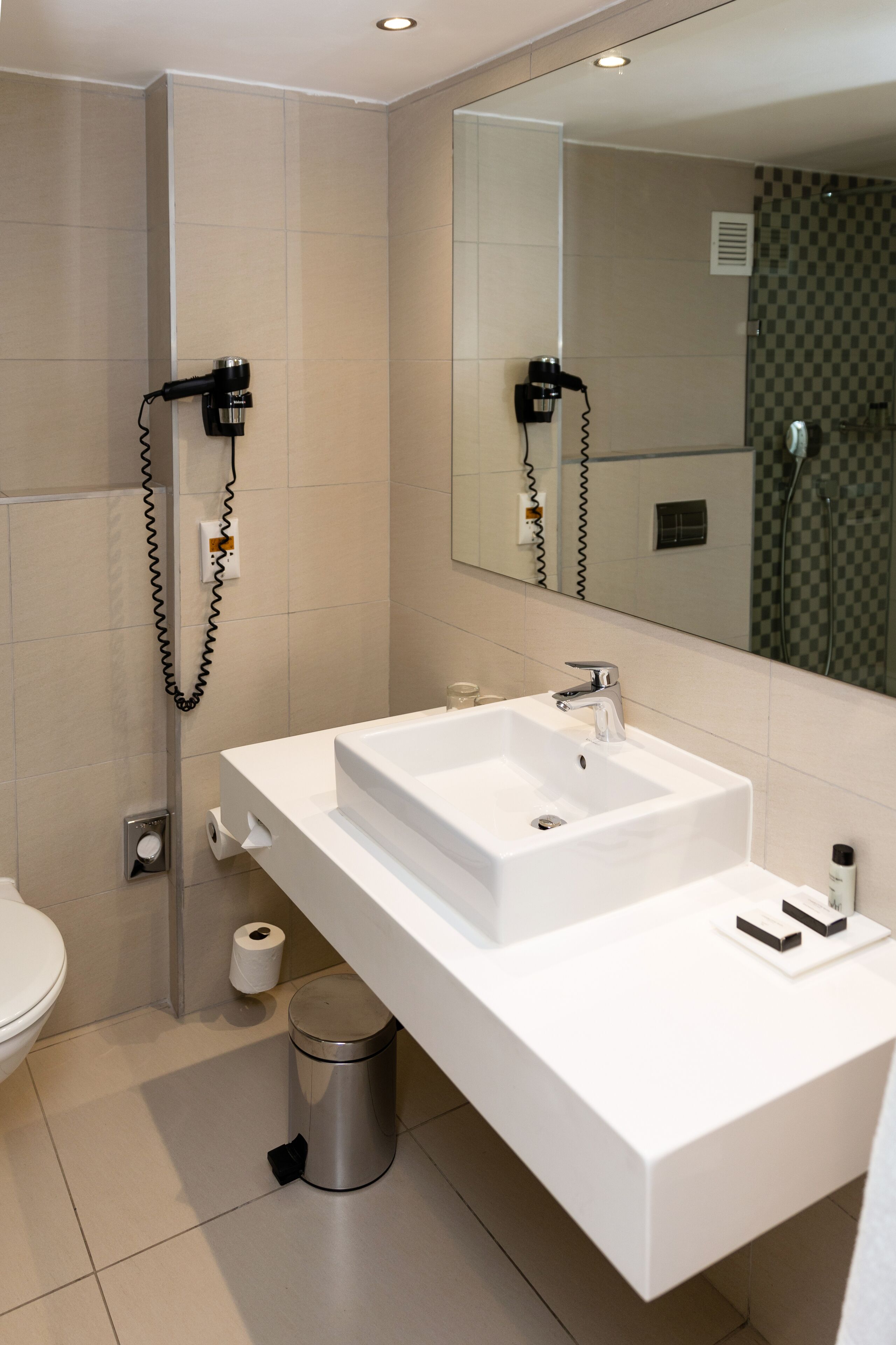 A modern bathroom with a white sink, mirror, and a hairdryer mounted on the wall.