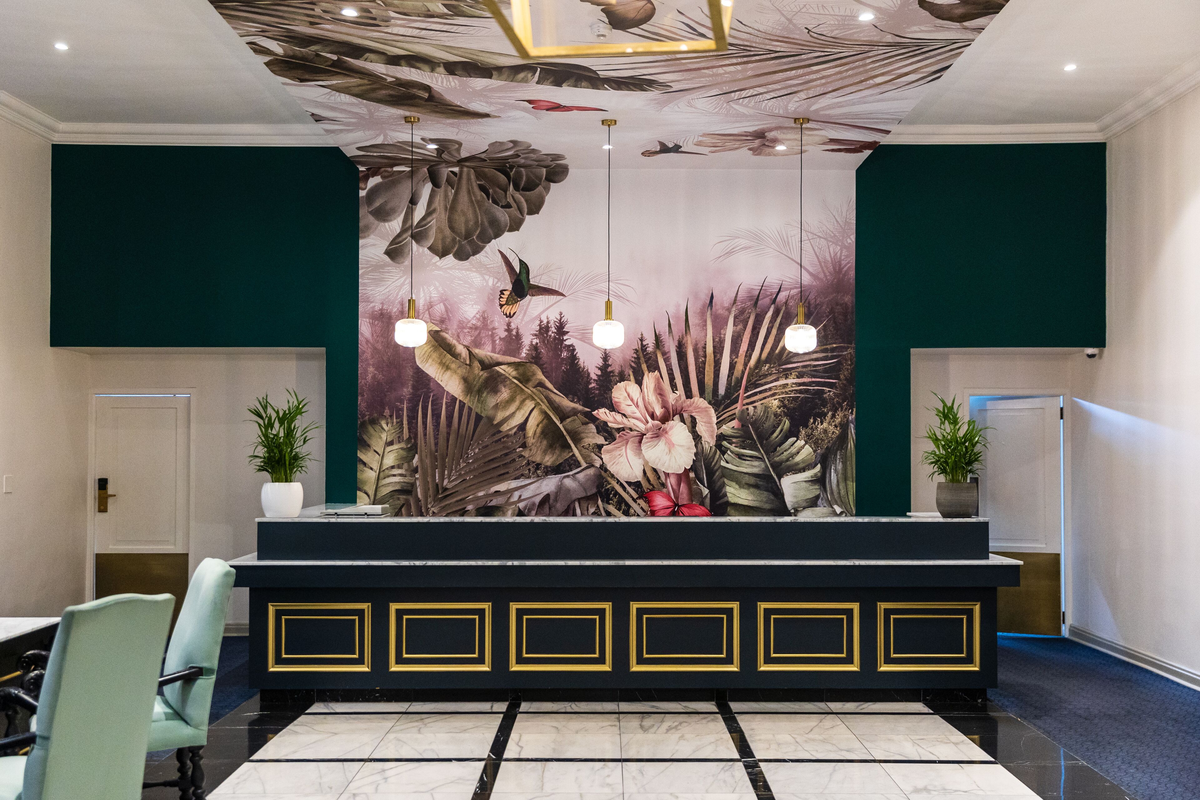 Uma área de recepção com balcão preto, paredes verdes e um grande mural floral na parede de fundo.