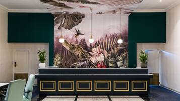 Uma área de recepção com balcão preto, paredes verdes e um grande mural floral na parede de fundo.