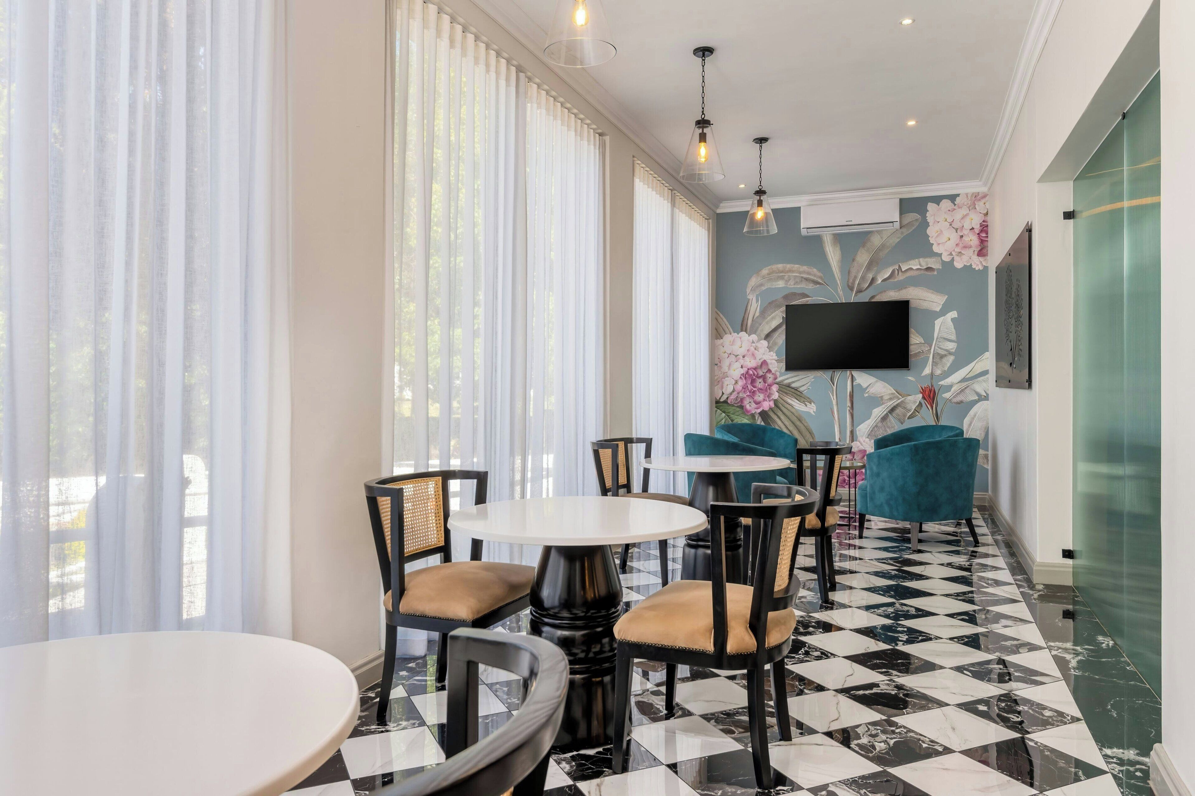 A hotel lobby with round tables and chairs, a flat-screen TV mounted on the wall, and a decorative wall mural.