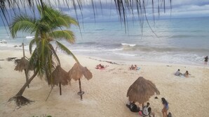 A beach with thatched umbrellas, palm trees, and people relaxing on the sand. - Casa Noa master suite 3 steps from the sea (Tulum)