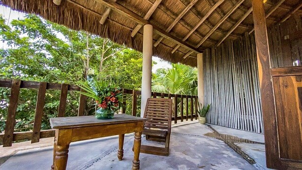 An outdoor seating area with a wooden table and bench, surrounded by a wooden fence and tropical vegetation. - Casa Noa master suite 3 steps from the sea (Tulum)