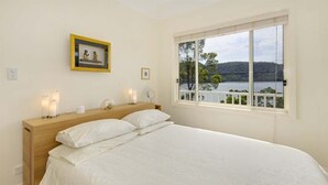 Ein Schlafzimmer mit einem großen Bett, einem Holz-Kopfteil, Nachttischlampen und einem Fenster mit Blick auf einen See und Hügel.
