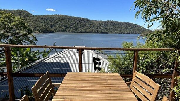 Eine Holzterrasse mit Tisch und Stühlen mit Blick auf einen See, mit einem Metalldach und einem Holzaushleger.