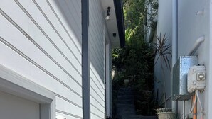Eine enge Treppe führt zu einem weißen Gebäude, ausgestattet mit einem Holzgeländer und Blumentöpfen am Fuß.