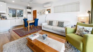 Ein modernes Wohnzimmer mit einer Couch, einem grünen Sessel, einem Couchtisch und einem Essbereich mit Tisch und Stühlen.